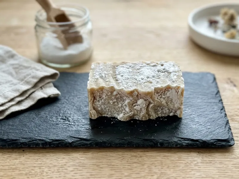 A rustic handmade soap bar dusted with white powder rests on a dark slate board.